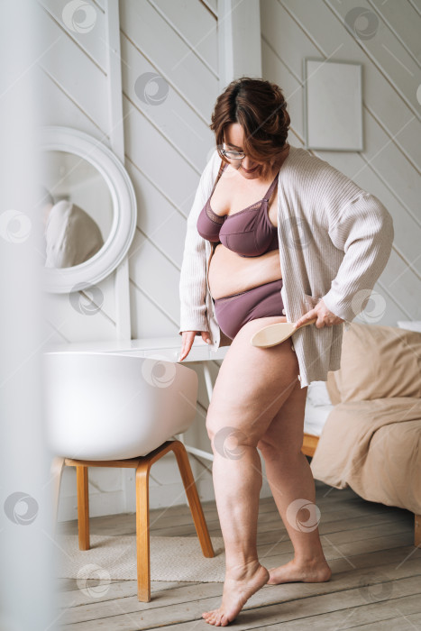 Скачать Женщина среднего возраста плюс размер в нижнем белье делает массаж тела сухой деревянной щеткой в ванной дома фотосток Ozero