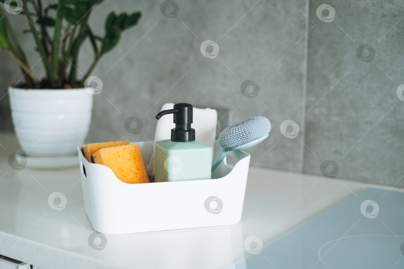 Скачать Кухонные чистящие средства щетка, жидкое мыло, губка для мытья посуды в контейнере на кухонном столе дома фотосток Ozero