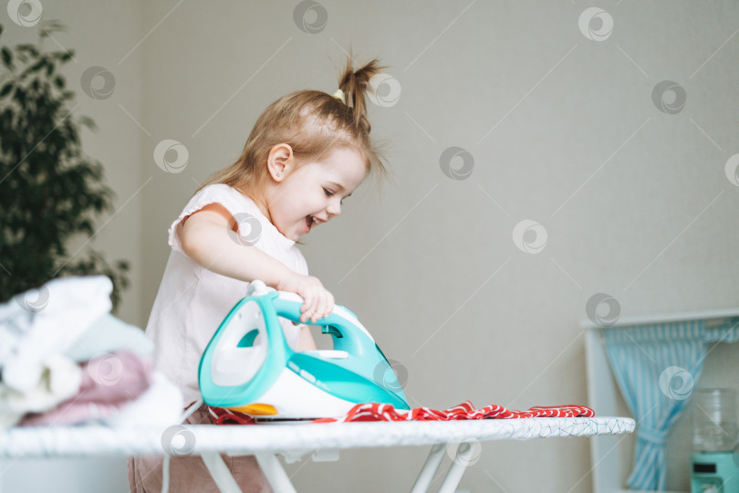Скачать Милая маленькая девочка играет и гладит одежду утюгом дома фотосток Ozero