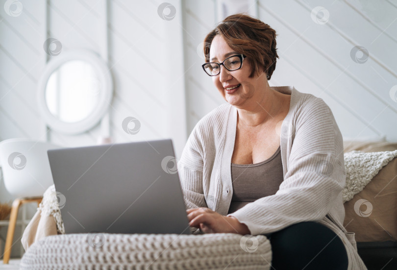 Скачать Улыбающаяся женщина средних лет плюс размер, работающая на ноутбуке дома фотосток Ozero