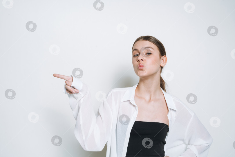 Скачать Молодая девушка-подросток в белой рубашке указывает на пустое место для копирования, изолированное на белом фоне background фотосток Ozero