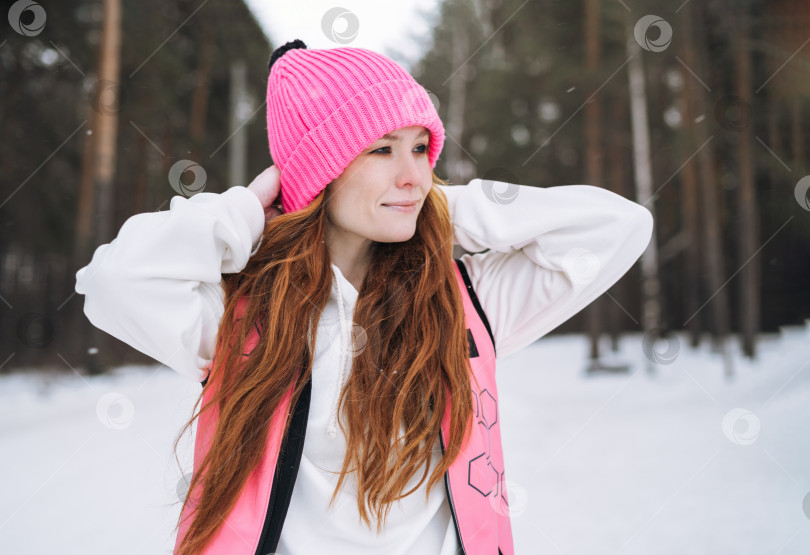 Скачать Молодая рыжеволосая женщина в розовой спортивной одежде бежит по зимнему заснеженному лесу фотосток Ozero