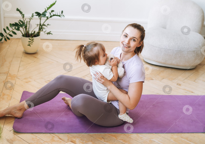 Скачать Молодая женщина, подтянутая мама с маленькой девочкой, занимается фитнесом на коврике дома фотосток Ozero