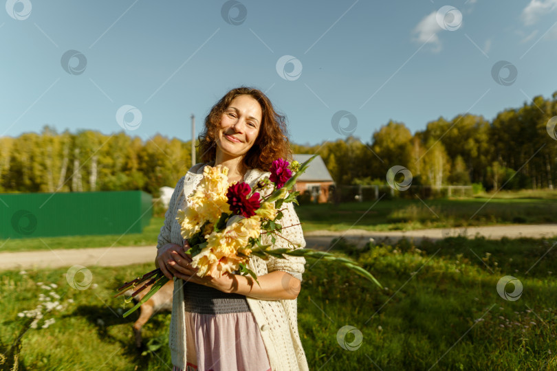 Скачать Улыбающаяся женщина с букетом цветов, наслаждающаяся спокойствием сельской жизни фотосток Ozero