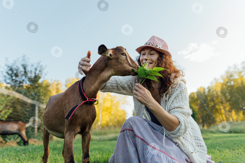 Скачать Улыбающаяся женщина в шляпе общается с козой в сельской местности фотосток Ozero