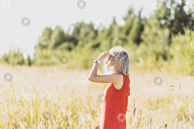 Скачать Молодая блондинка в ярком платье стоит посреди поля с раскинутыми руками. Счастье, свобода, лето, отпуск фотосток Ozero