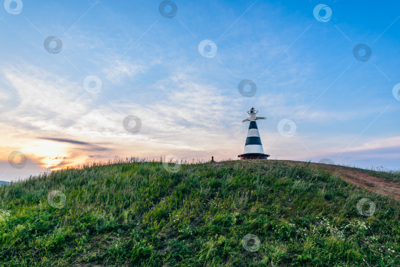 Скачать Маяк с указателем на холме в лучах заходящего солнца фотосток Ozero