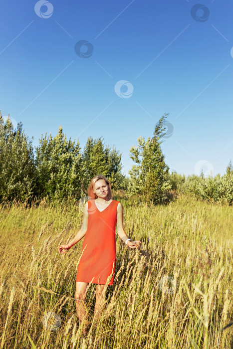 Скачать Молодая блондинка в ярком платье стоит посреди поля с раскинутыми руками. Счастье, свобода, лето, отпуск фотосток Ozero