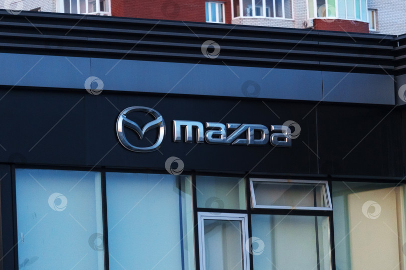 Скачать Тюмень, Россия - 18 марта 2024 года: Логотип Mazda на видном месте. Логотип узнаваем и дополняет фирменный стиль зданий. фотосток Ozero