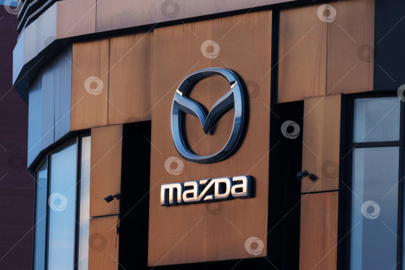 Скачать Тюмень, Россия - 18 марта 2024 года: Логотип Mazda размещен на фасаде здания, выделяясь на общем фоне. фотосток Ozero