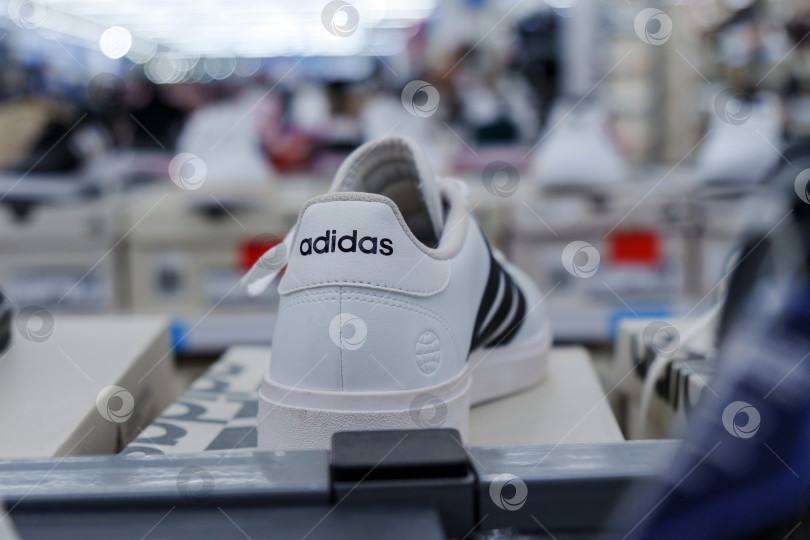 Скачать Тюмень, Россия - 11 августа 2024 года: Белая спортивная обувь adidas с черными полосками представлена на видном месте в розничной торговле. фотосток Ozero