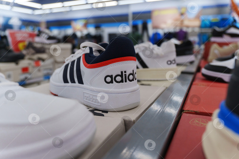 Скачать Тюмень, Россия - 11 августа 2024 года: Белая спортивная обувь adidas с черными полосками представлена на видном месте в розничной торговле. фотосток Ozero