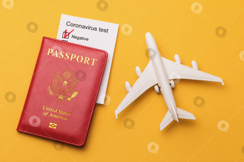 Скачать Игрушечный самолетик, американский паспорт и результаты теста на коронавирус на желтом фоне, вид сверху фотосток Ozero