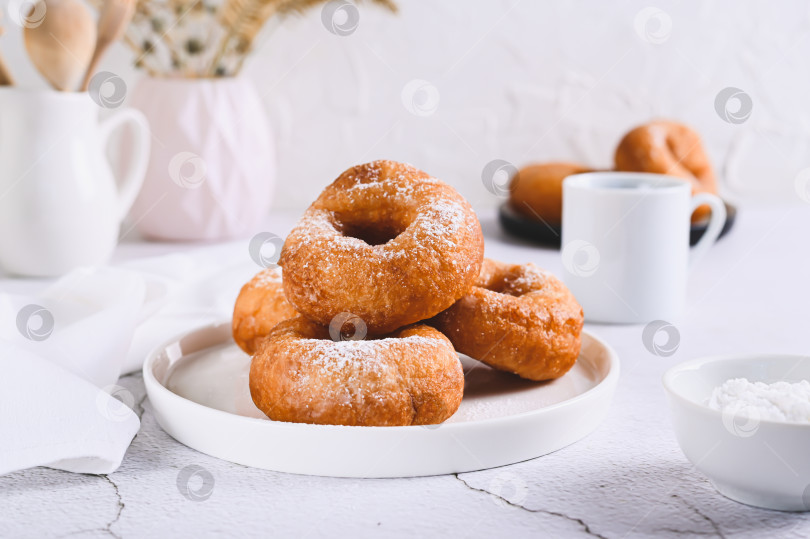 Скачать Вкусные пончики в сахарной пудре на тарелке на белом столе фотосток Ozero