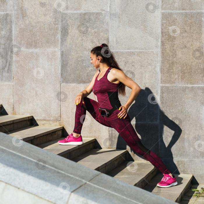 Скачать Молодая женщина в спортивной одежде выполняет упражнения на открытом воздухе, слушая музыку фотосток Ozero