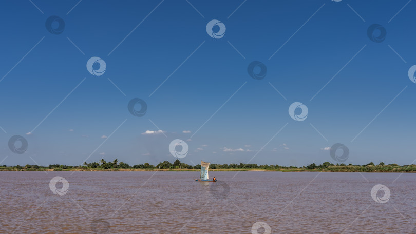 Скачать Каноэ с парусом плывет по спокойной красно-коричневой реке. фотосток Ozero