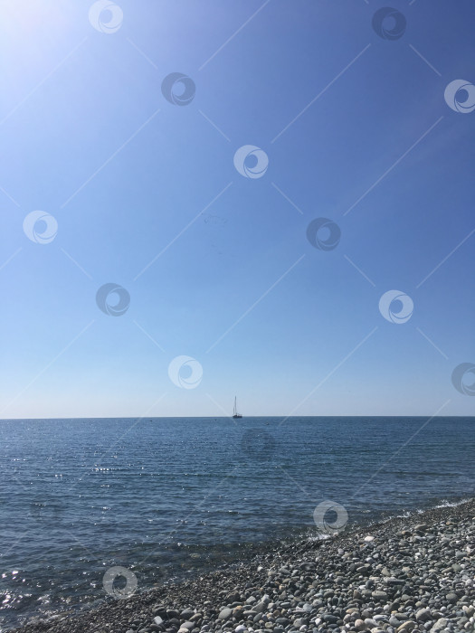 Скачать Море. Каменный пляж и голубое небо без облаков. Корабль находится далеко на горизонте. Мобильная фотография фотосток Ozero