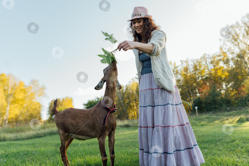 Скачать Улыбающаяся женщина в шляпе общается с козой в сельской местности фотосток Ozero