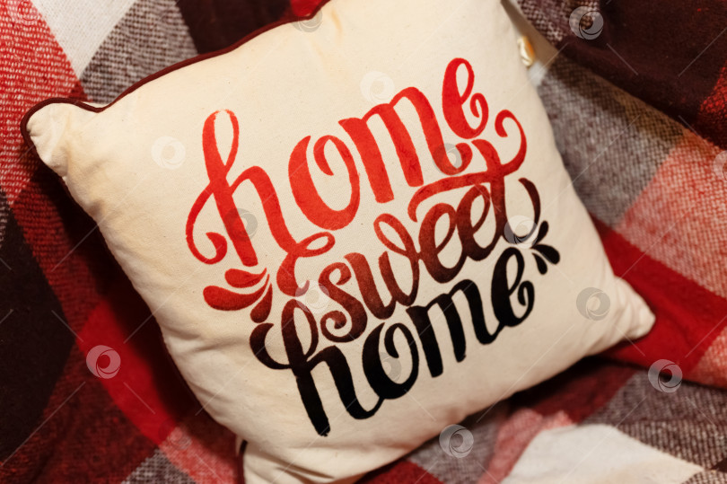 Скачать рождественское время. уютная удобная мягкая диванная подушка или валик или подушечка с надписью "home sweet home" на красном шерстяном пледе в клетку. новогодний домашний декор интерьера фотосток Ozero
