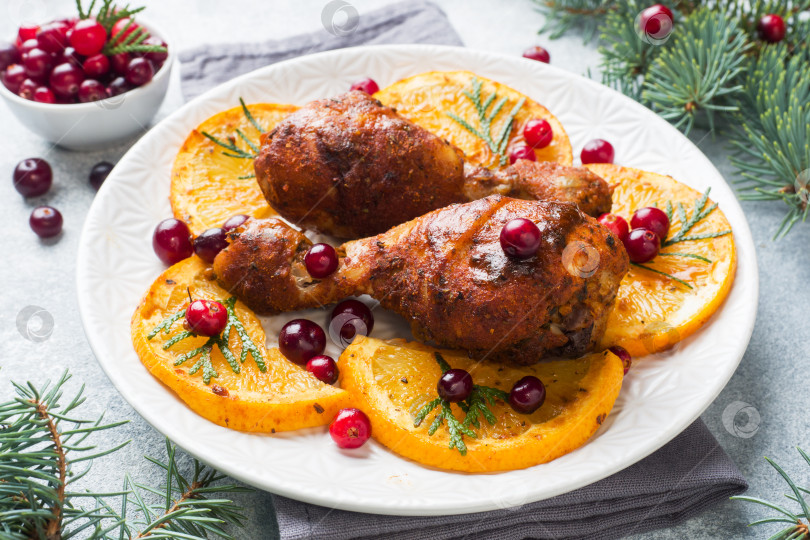 Скачать Запеченная куриная голень с апельсинами и клюквой на светло-сером фоне. Рождественский праздничный стол с украшениями. фотосток Ozero