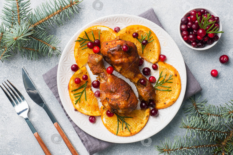 Скачать Запеченная куриная ножка с апельсинами и клюквой на светло-сером фоне. Рождественский праздничный стол с украшениями. фотосток Ozero