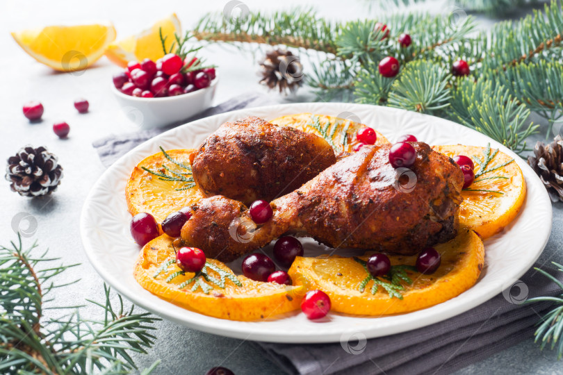 Скачать Запеченная куриная ножка с апельсинами и клюквой на светло-сером фоне. Рождественский праздничный стол с украшениями. фотосток Ozero