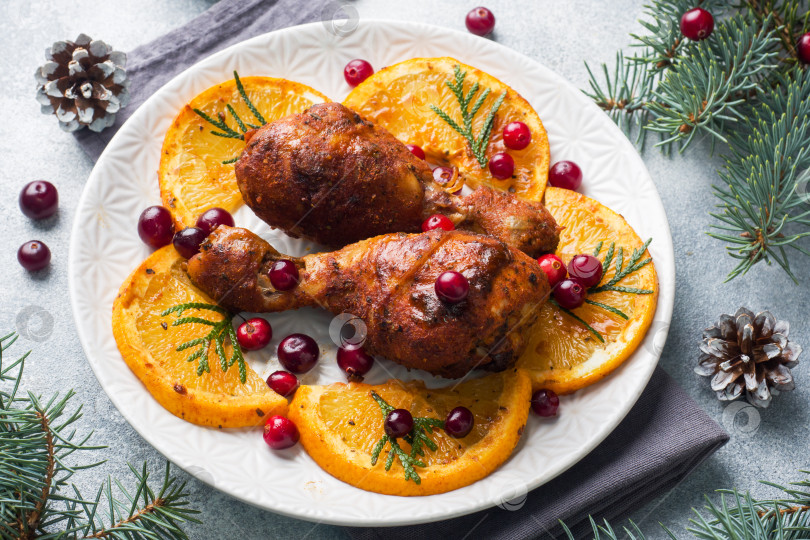 Скачать Запеченная куриная ножка с апельсинами и клюквой на светло-сером фоне. Рождественский праздничный стол с украшениями. фотосток Ozero