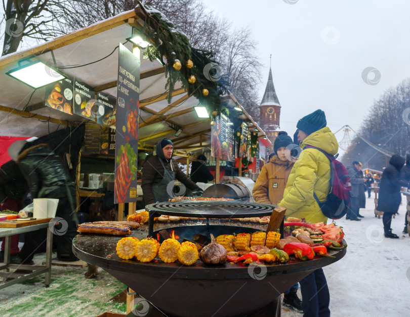 Скачать Праздничная ярмарка на улице зимой в городе. Приготовление овощей на гриле во время праздничных мероприятий фотосток Ozero