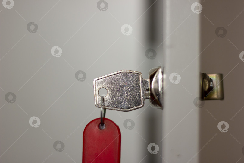 Скачать Металлический офисный ключ с красным брелоком в замке крупным планом, горизонтальное фото фотосток Ozero
