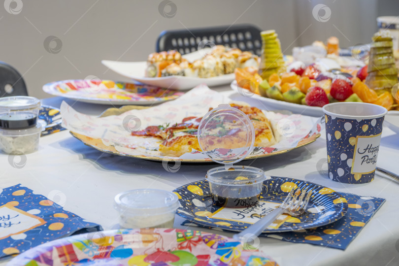 Скачать На банкетном столе стоят тарелки с недоеденной едой - ломтиками пиццы, фруктовыми нарезками из различных фруктов, соусом. фотосток Ozero