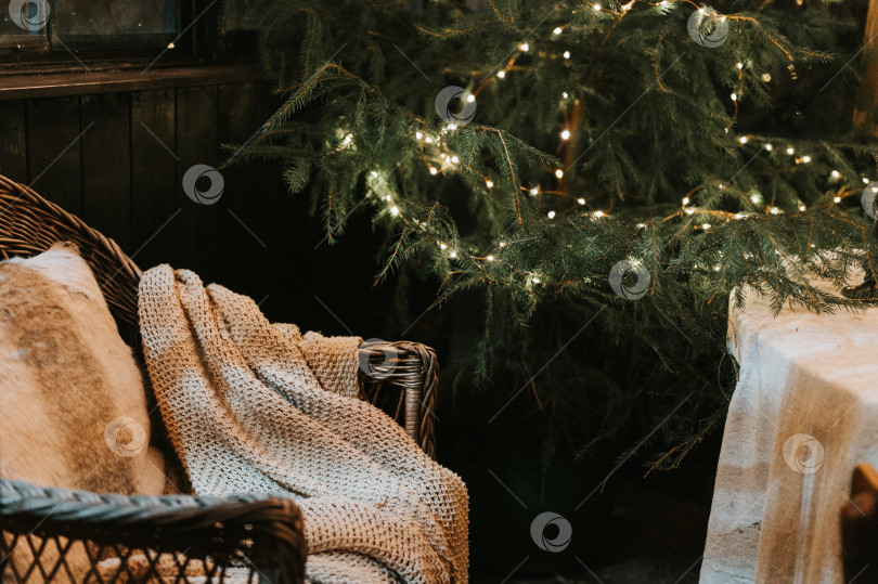Скачать время Рождества и нового года. уютное кресло или плетеное мягкое кресло с удобным вязаным пледом и меховой подушкой рядом с украшенной рождественской елкой со светящимся светом сезон зимних праздников дома фотосток Ozero