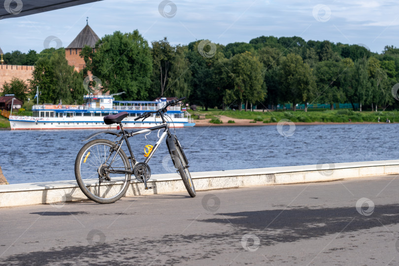 Скачать Новгород, Новгородская область, Россия - 30 июля 2024 года. Велосипед стоит на набережной с видом на реку Волхов. Выборочный показ. фотосток Ozero