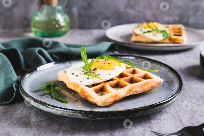 Скачать Бельгийские вафли с жареным яйцом, рукколой и специями на тарелке на столе фотосток Ozero