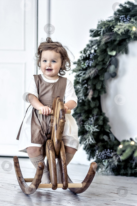 Скачать Маленькая девочка качается на деревянной лошадке в комнате на фоне рождественских украшений. фотосток Ozero