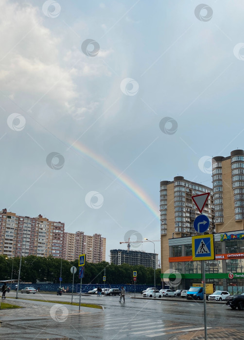 Скачать Радуга после дождя в городе над многоэтажными домами. Городская улица, дорога, тротуар после дождя фотосток Ozero