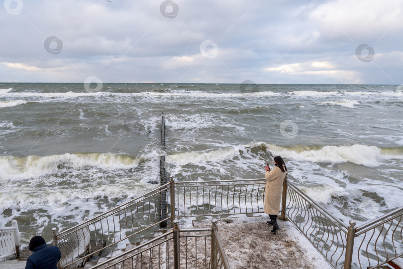 Скачать Девушка фотографирует морские волны. Пасмурная ветреная погода на морском курорте. фотосток Ozero