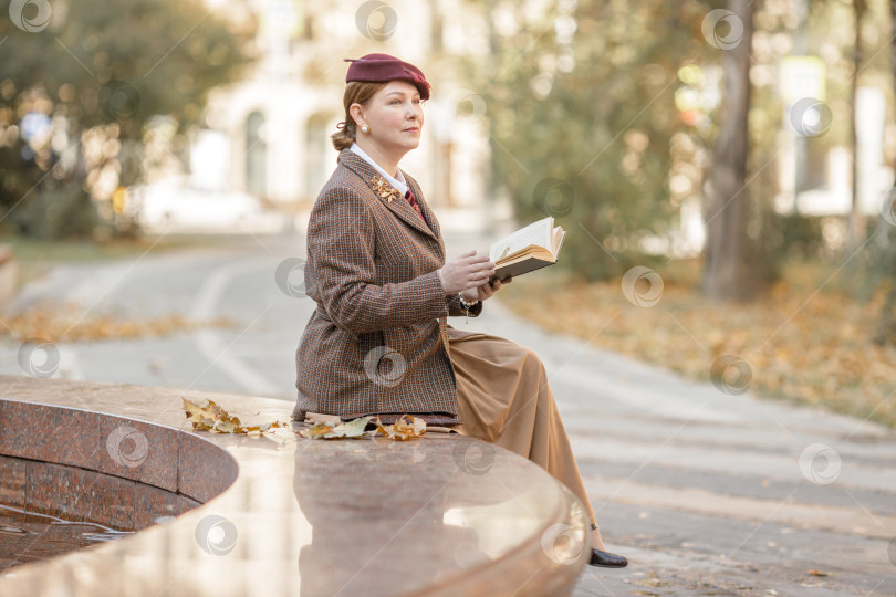 Скачать Брюнетка в винтажной одежде и шляпе с книгой в руках сидит на скамейке в осеннем парке. Ретро-стиль фотосток Ozero