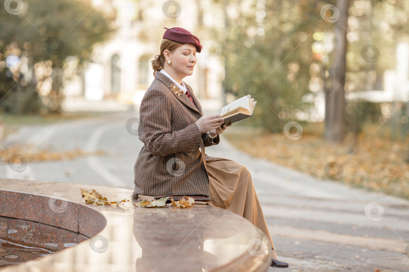 Скачать Брюнетка в винтажной одежде и шляпе с книгой в руках сидит на скамейке в осеннем парке. Ретро-стиль фотосток Ozero