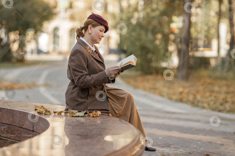 Скачать Брюнетка в винтажной одежде и шляпе с книгой в руках сидит на скамейке в осеннем парке. Ретро-стиль фотосток Ozero