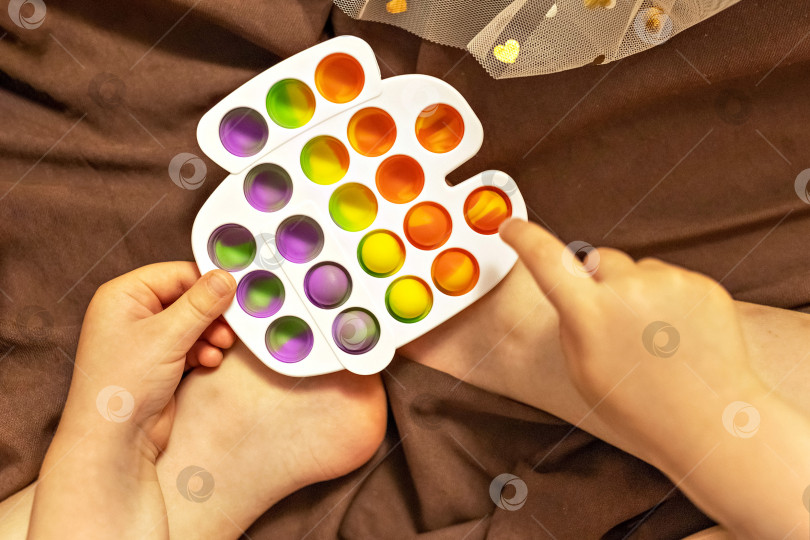 Скачать Pop it - это разноцветная игрушка-антистресс в детских руках. Игра с пузырями. Игрушки-антистрессы. фотосток Ozero