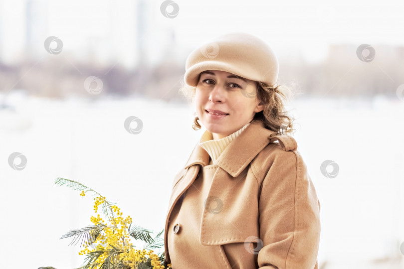 Скачать Портрет молодой женщины в бежевом пальто и шляпе с букетом мимозы в руках. Весна, Международный женский день 8 марта фотосток Ozero