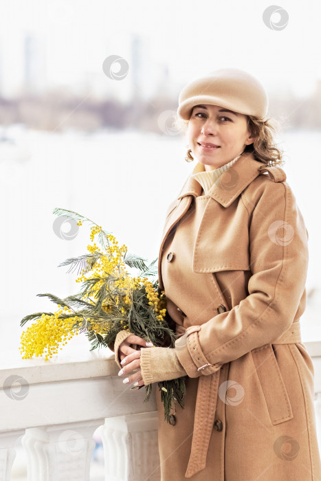 Скачать Портрет молодой женщины в бежевом пальто и шляпе с букетом мимозы в руках. Весна, Международный женский день 8 марта фотосток Ozero