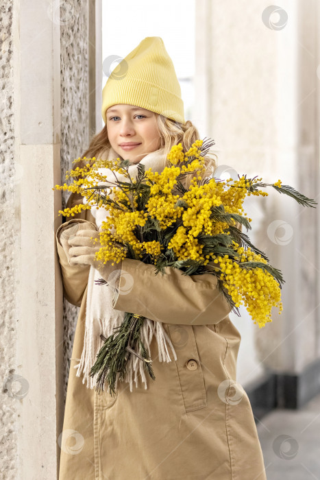 Скачать Портрет девушки в бежевом пальто с букетом мимозы в руках в парке. Весна, Международный женский день 8 марта фотосток Ozero