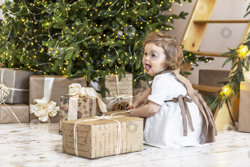 Скачать Маленькая девочка у рождественской елки с коробками подарков. Распаковка подарков, эмоции,детство. фотосток Ozero