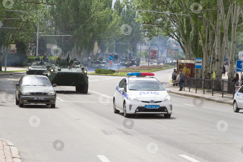 Скачать Донецк, Донецкая Народная Республика, Украина – 9 мая 2019 года: Полицейские машины проезжают впереди колонны советской военной бронетехники. Улица Артема, центральный район Донецка. Окончание парада в честь Дня Победы. фотосток Ozero