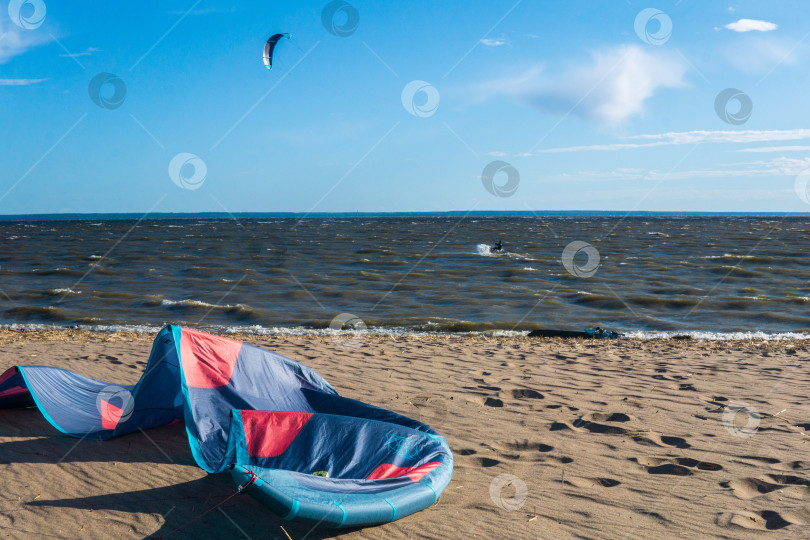 Скачать тяговый воздушный змей лежит на берегу, в море виден кайтбордист, которого тянет по воде другой силовой воздушный змей фотосток Ozero