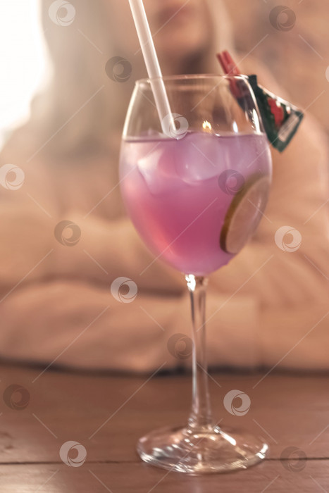 Скачать Фруктово-розовый коктейль с ломтиком лайма на столике в кафе. На заднем плане размытая фигура женщины, сидящей за столом фотосток Ozero