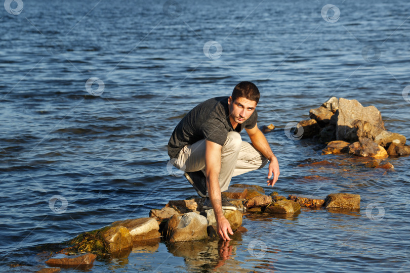Скачать Человек сидит на прибрежных камнях. фотосток Ozero
