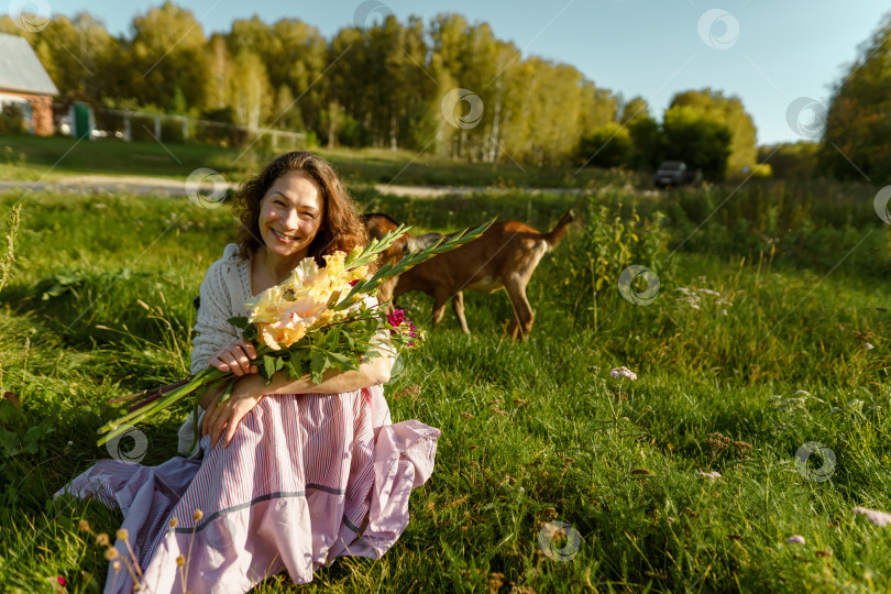 Скачать Летний день на ферме: Женщина с цветами и козами, наслаждающаяся простой жизнью фотосток Ozero