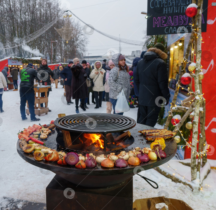 Скачать Праздничная ярмарка на улице зимой в городе. Приготовление овощей на гриле во время праздничных мероприятий фотосток Ozero